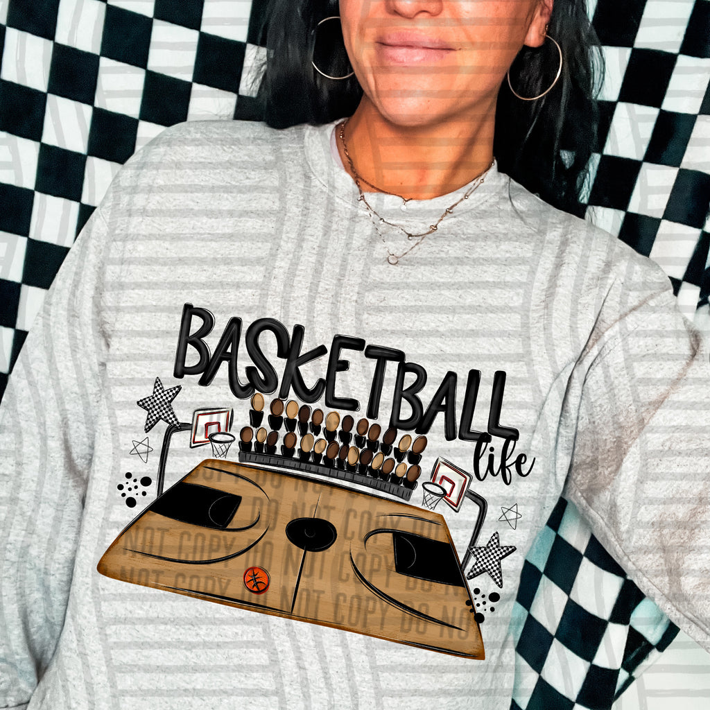 A person wearing a light gray heathered sweatshirt with a graphic print that says 'BASKETBALL life' above a stylized basketball court and hoops design. The background is a black and white checkered pattern.
